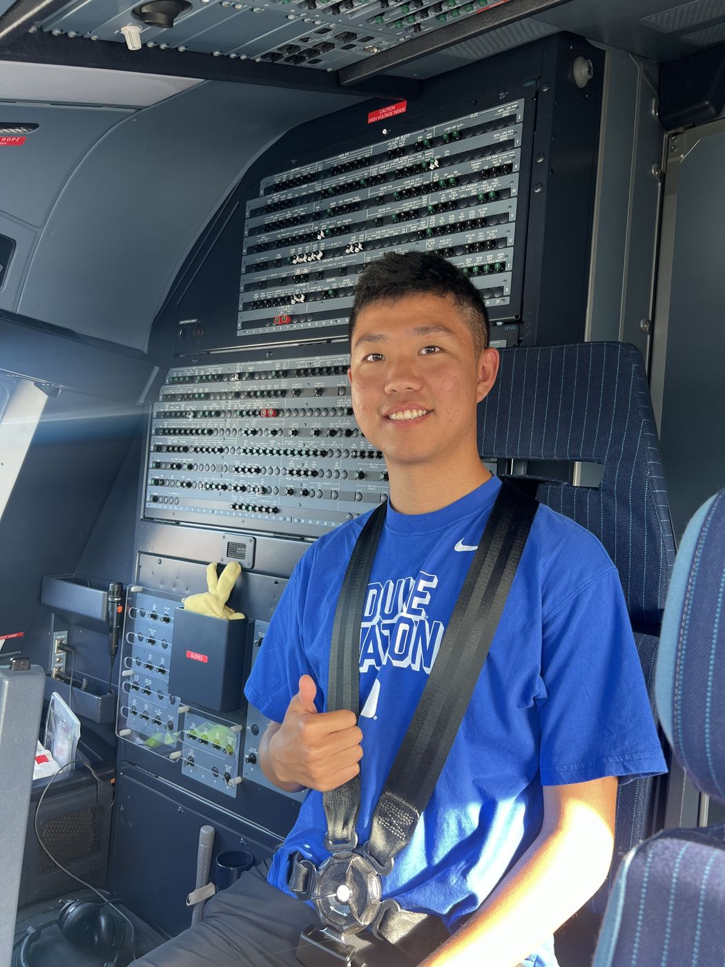 Thomas giving a thumbs-up in an airliner cockpit, in front of rows of circuit breakers