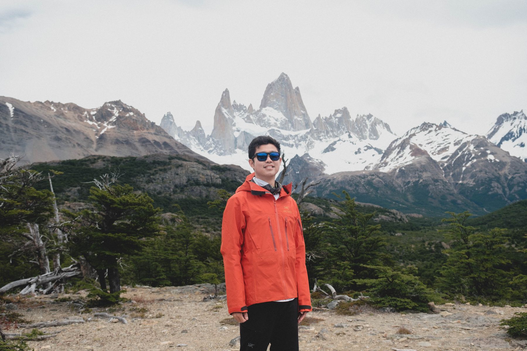 Thomas in a red jacket in front of the jagged, snow-covered peaks of Mount Fitz Roy