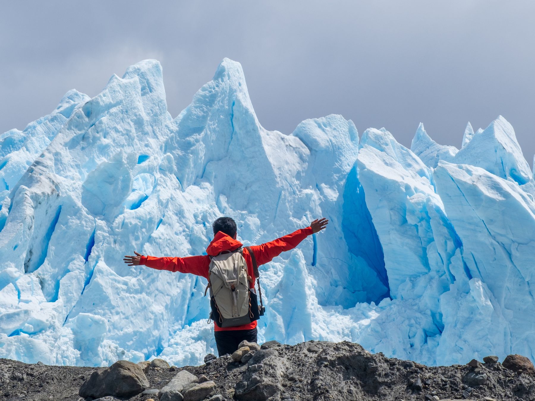 Thomas with arms outstretched in front of the blue ice wall of the Perito Moreno Glacier