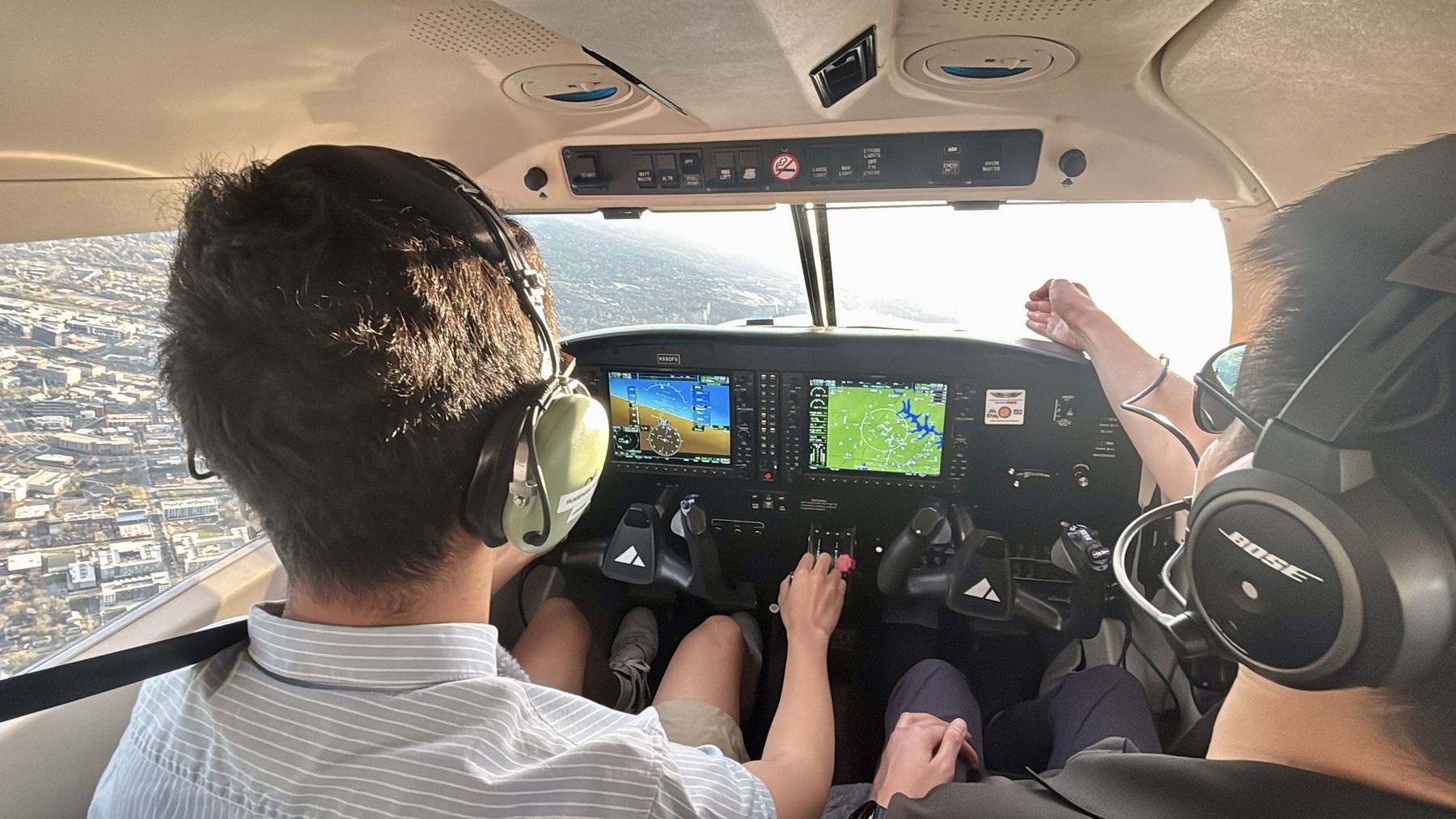 View from the back seat of a small aircraft cockpit in flight, with a student at the controls