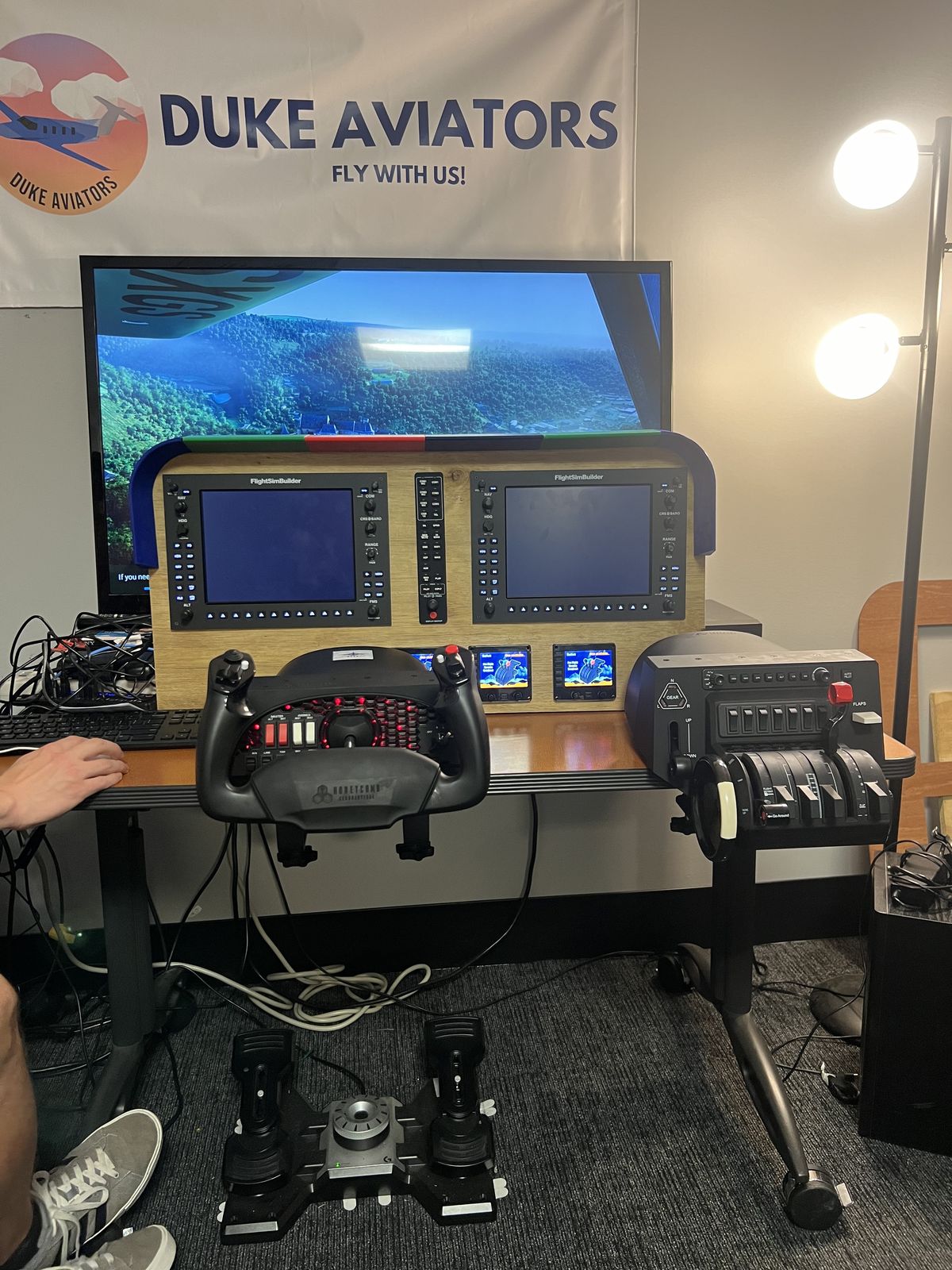 The Cessna 172 simulator: a large screen, instrument-panel housing with two displays, yoke, throttle quadrant and rudder pedals, under a Duke Aviators banner
